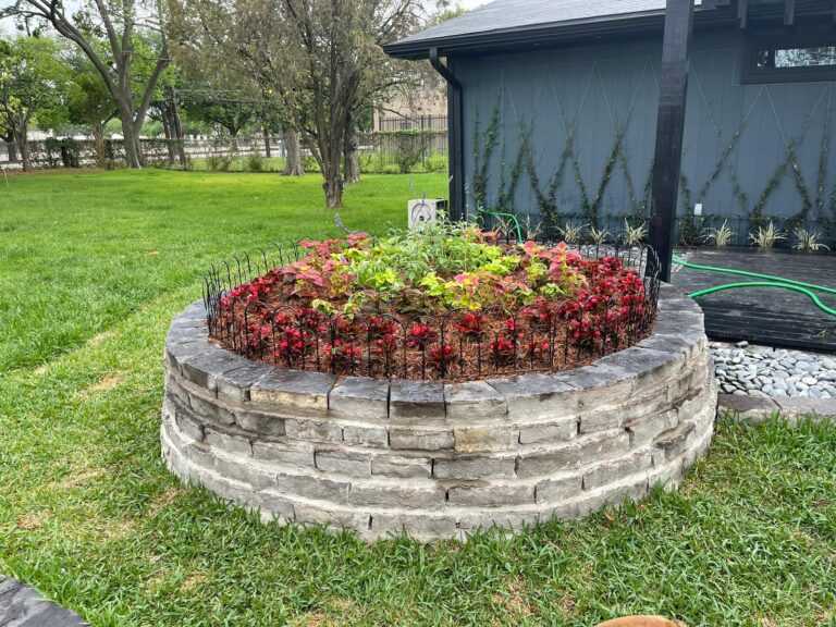 A circular bed of red seasonal flowers set into a green lawn