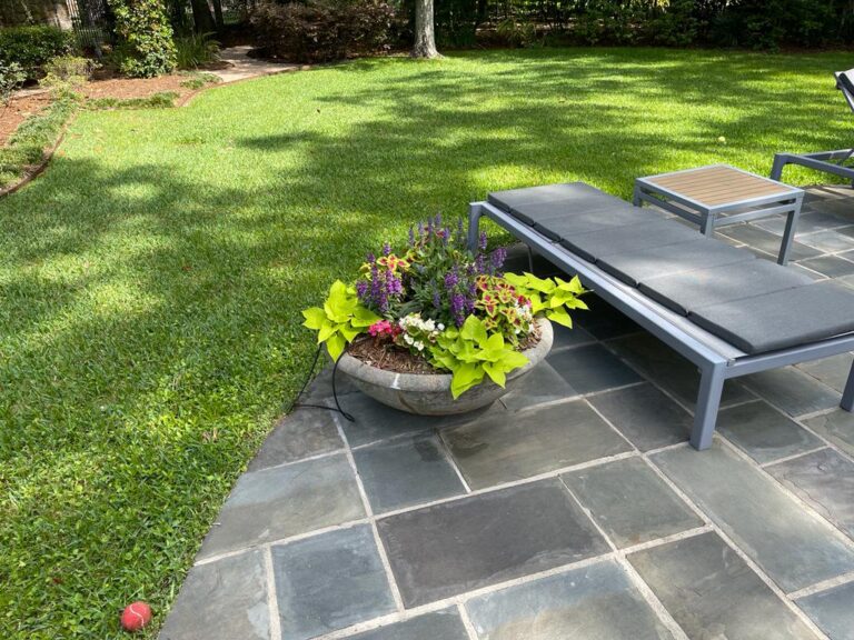 A closely mown, edged green lawn with a bench under mature trees