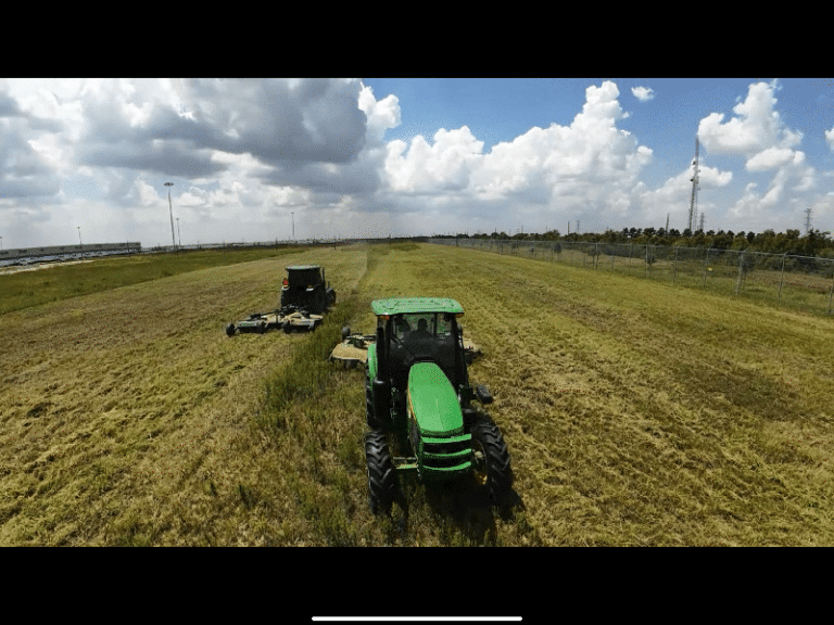 A tractor cutting tall grass on a large lot